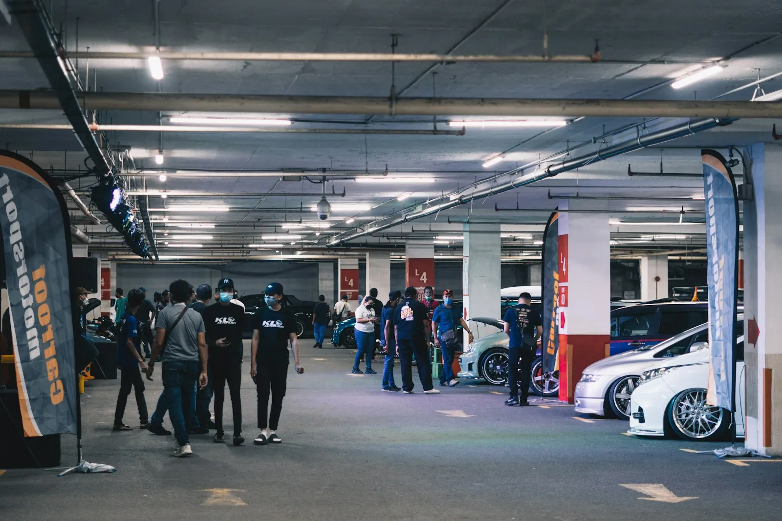 Visitors among cars and sponsor banners at an indoor car event